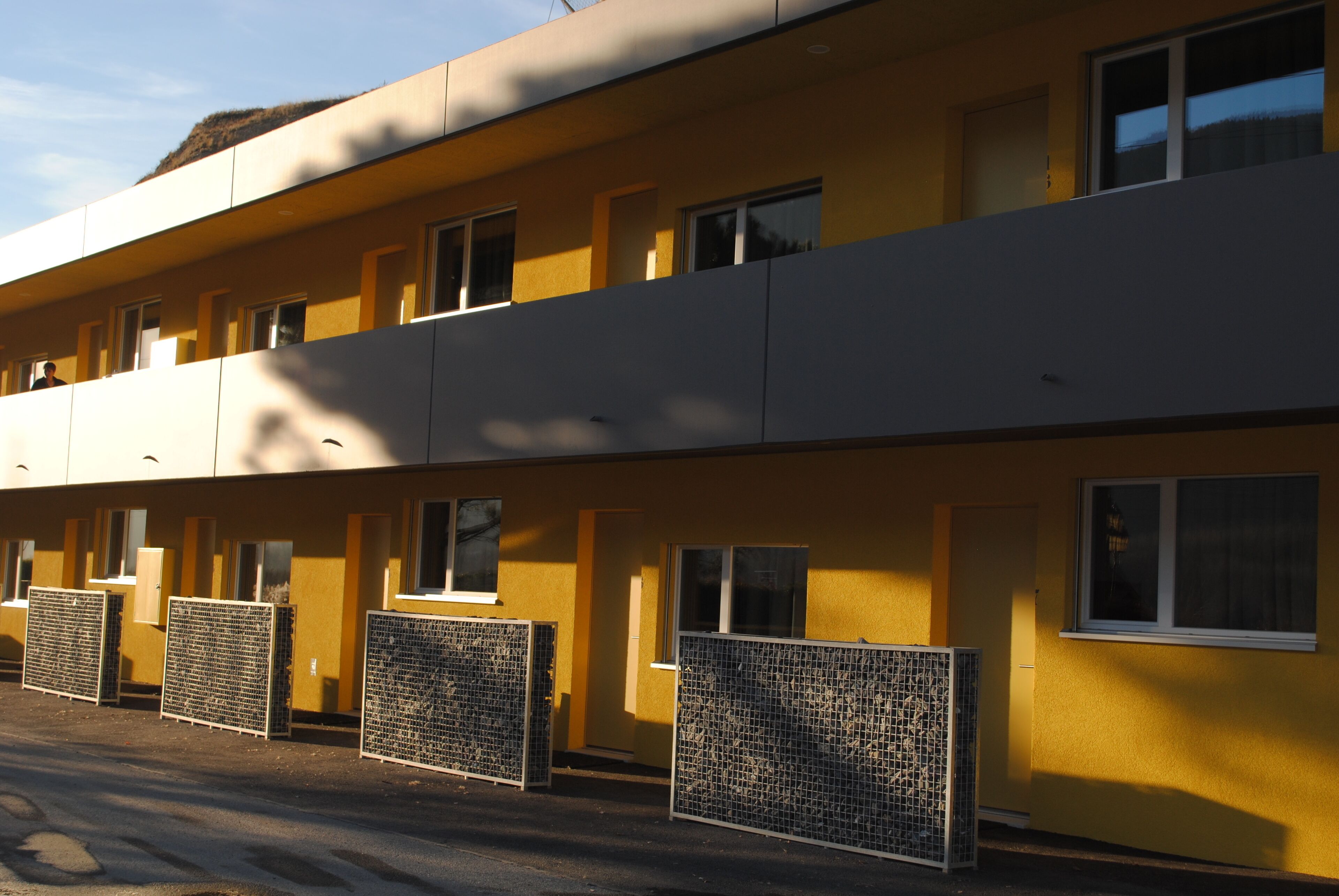 A multi-story building with a yellow facade, multiple windows, and several air conditioning units in front.