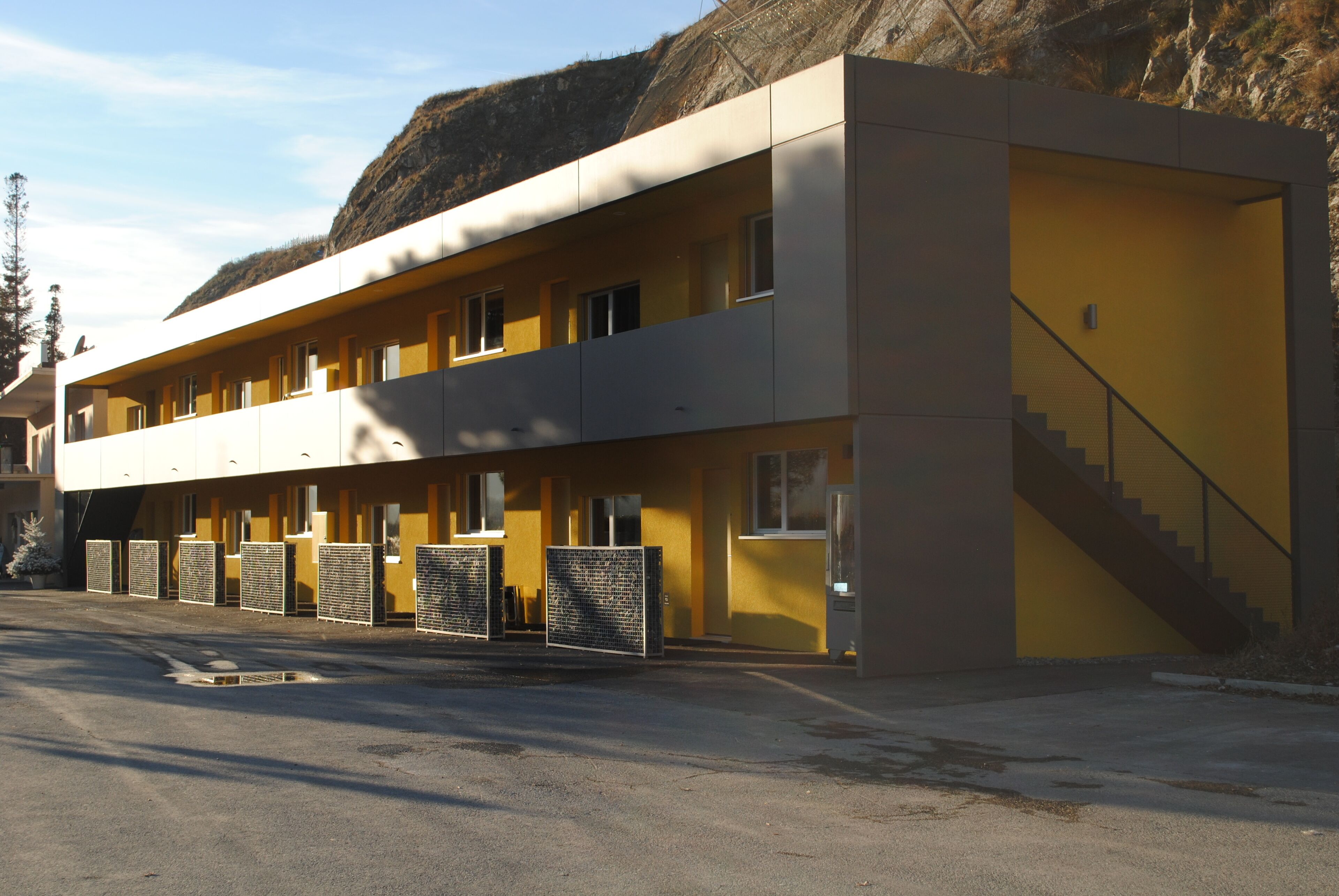 A two-story motel with a yellow facade, a staircase to the upper level, and a parking lot in front.