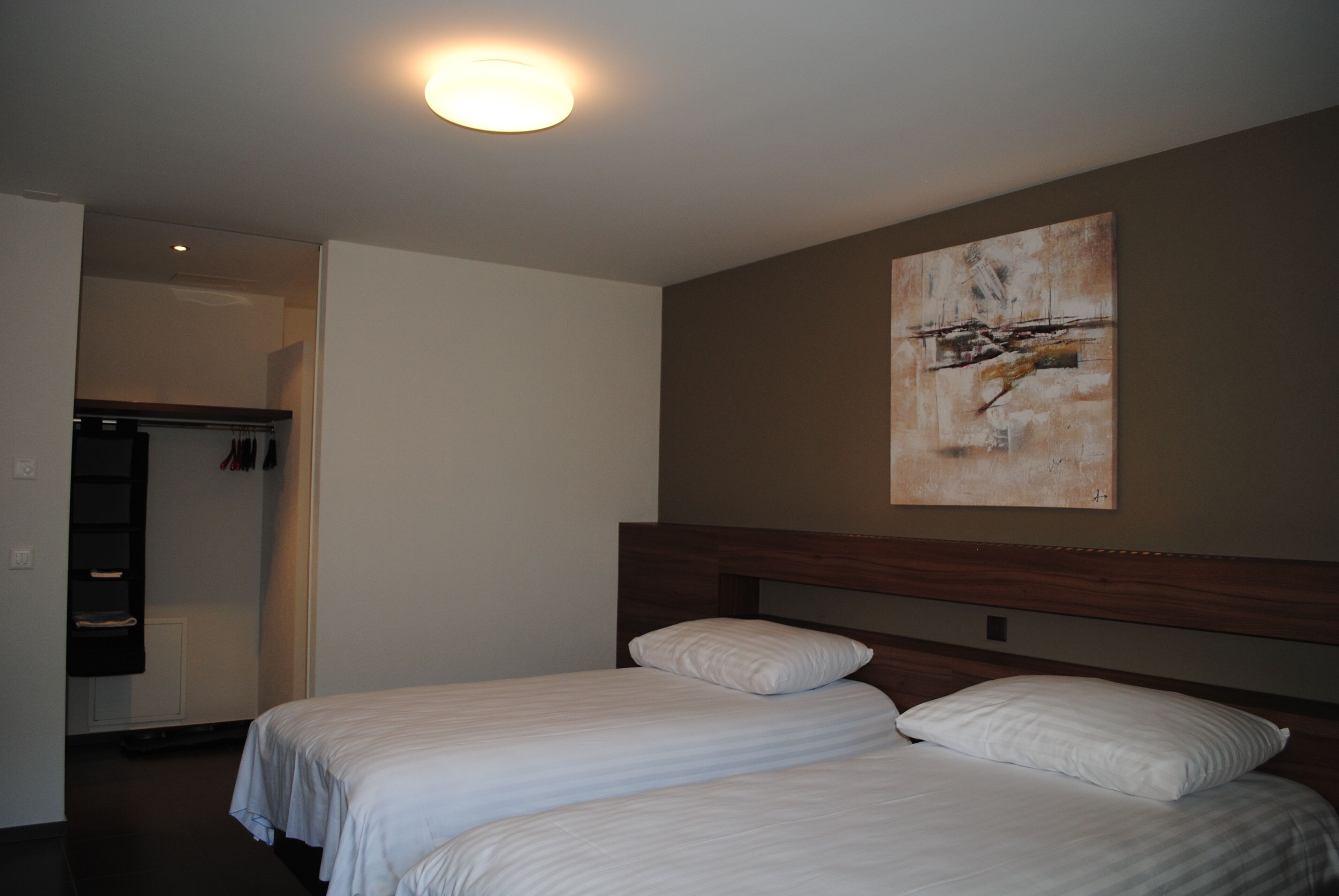 Ein Hotelzimmer mit zwei Einzelbetten, einem Holzkopfteil, einer Deckenleuchte und einem Gemälde an der Wand.