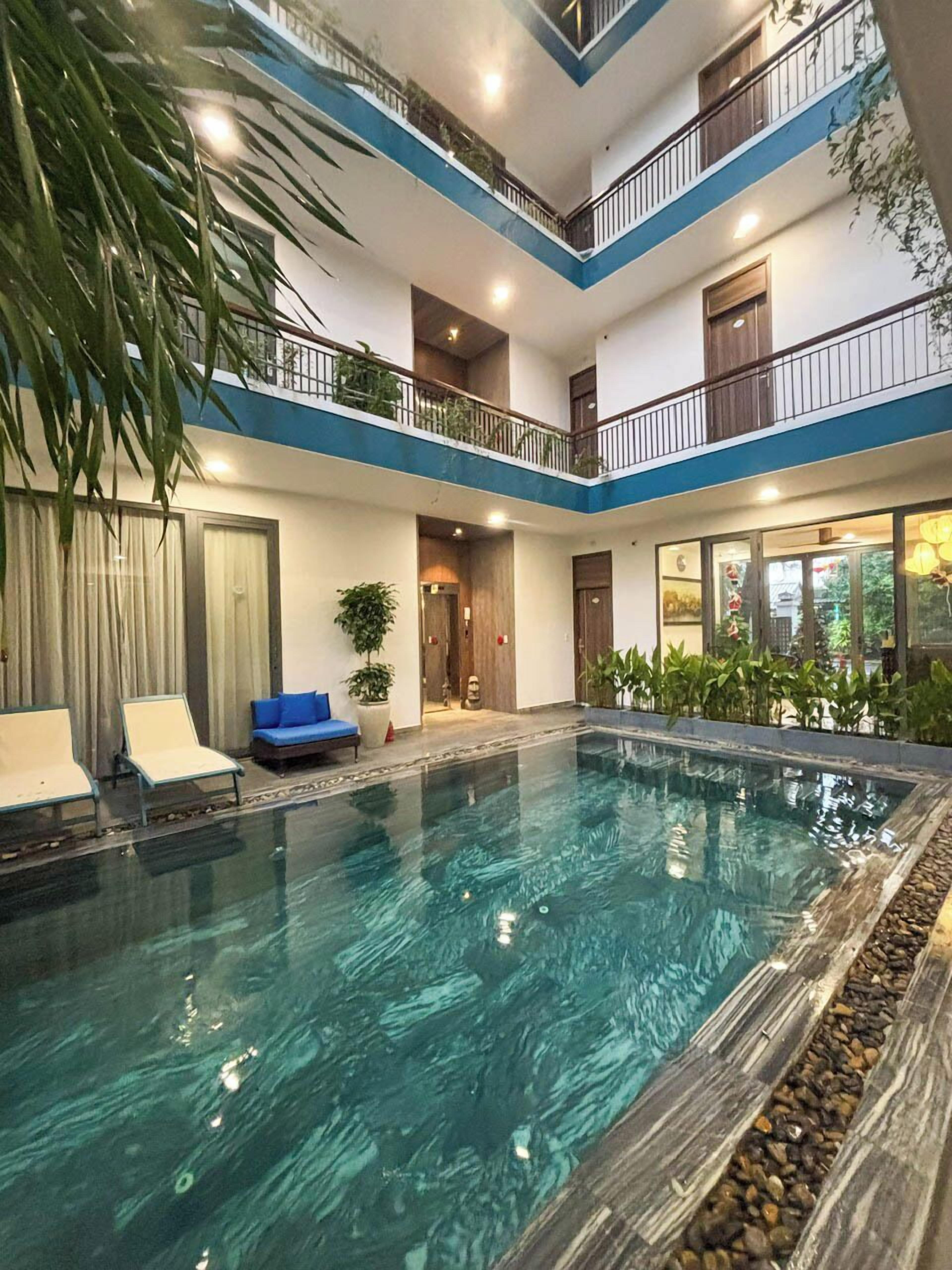 Una piscina cubierta de varios niveles con agua cristalina, rodeada de sillones de descanso y plantas en macetas.