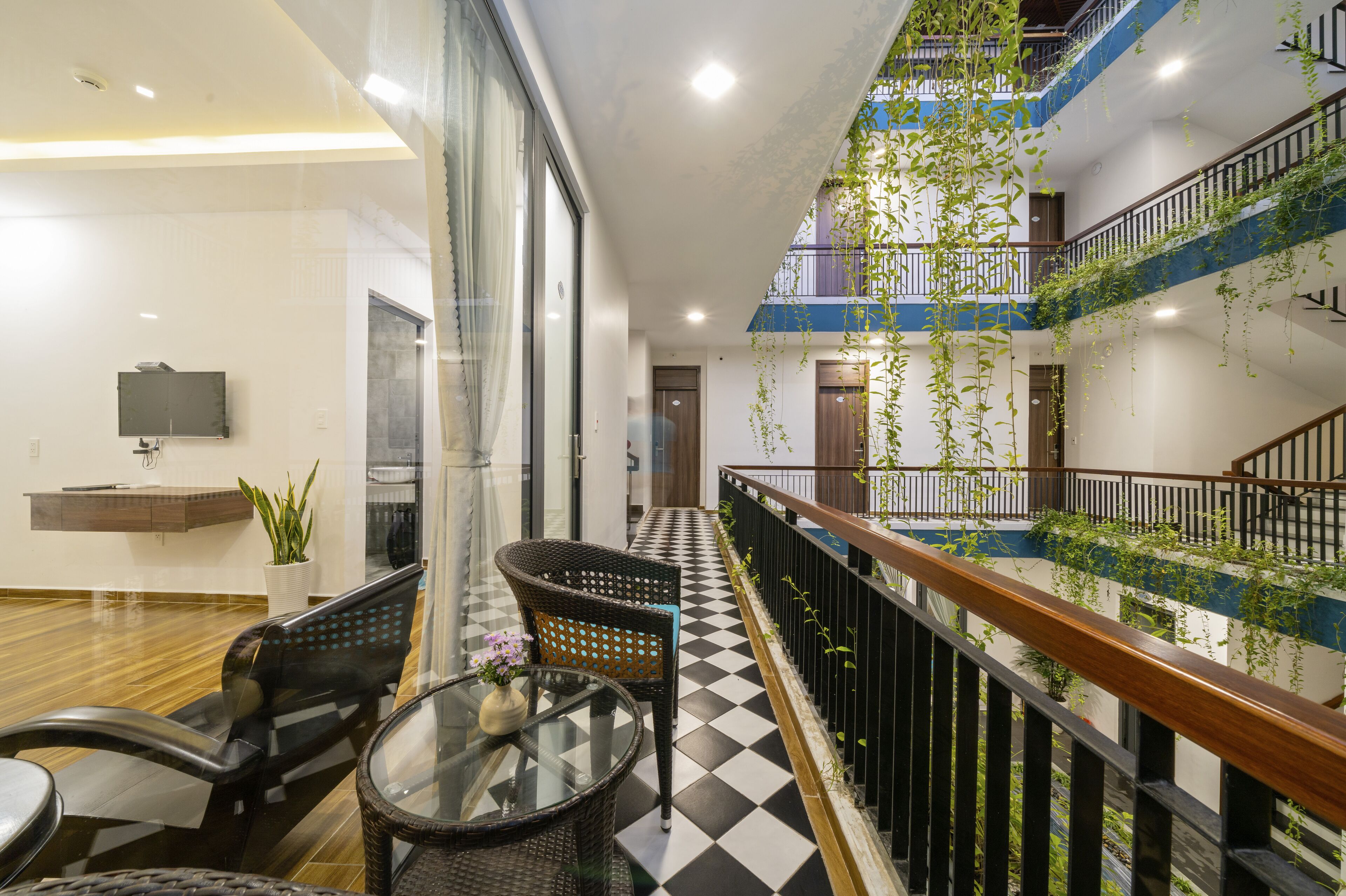 En modern hotellobby med ett rutmönstrat golv, svarta möbler i rotting, ett glasbord och en krukväxt.