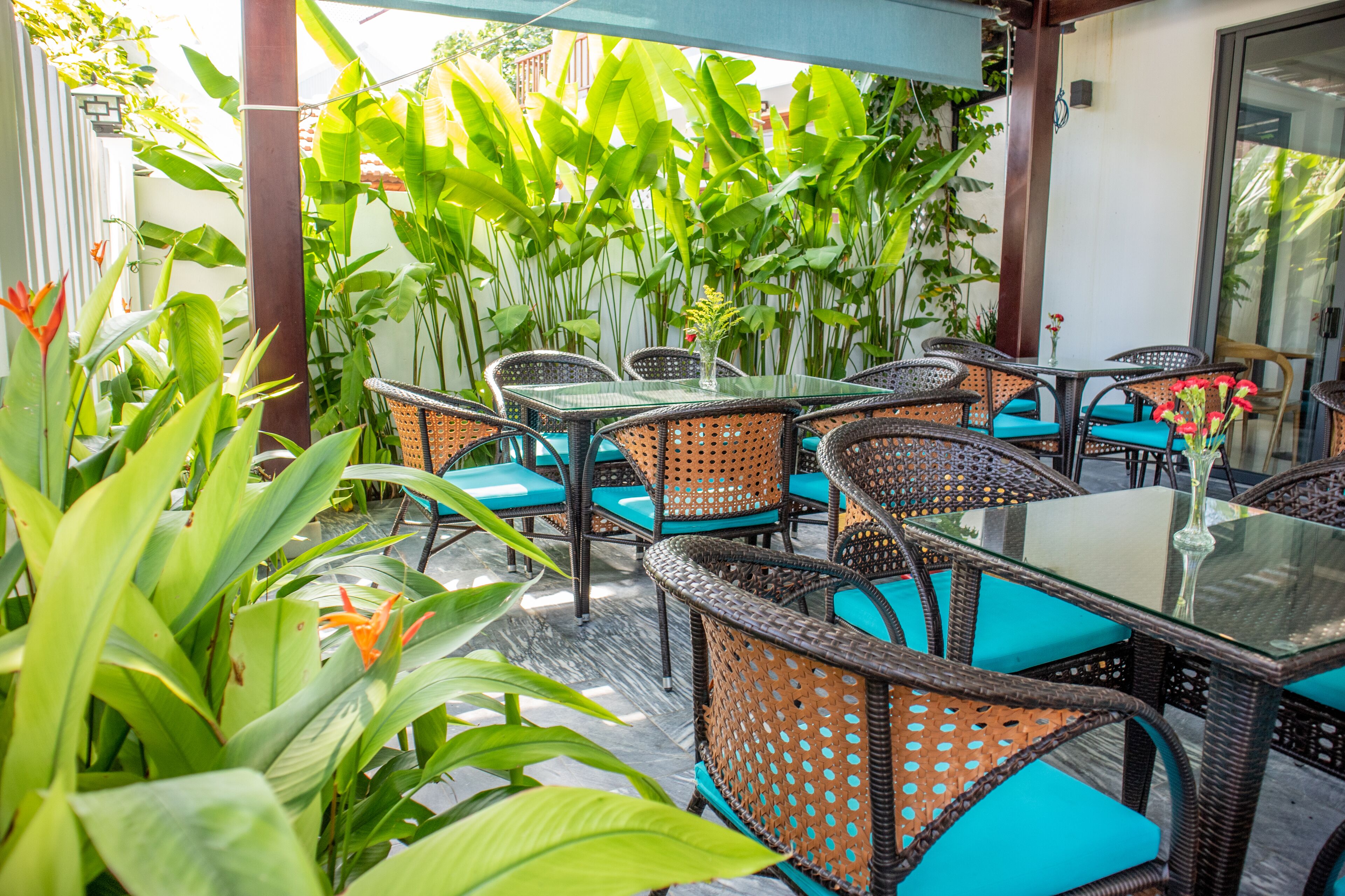 Ein Terrassenbereich im Freien mit Korbmöbeln und Glastischen, umgeben von üppigem Grün.