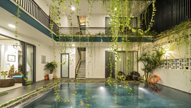 Piscina interior ampla, com design moderno, rodeada por plantas e uma escadaria que leva a um andar superior.