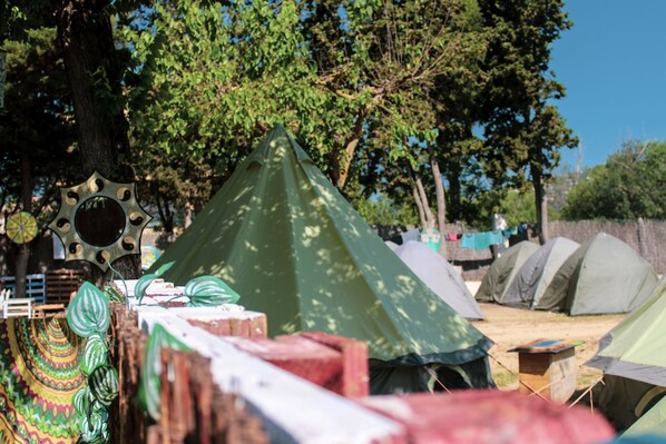 Un camping con varias tiendas de campaña, una valla de madera y árboles al fondo.