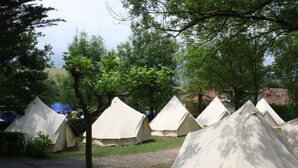 Una hilera de tiendas blancas en un camping, con árboles al fondo.