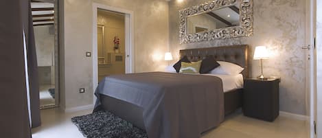 A modern bedroom with a large bed, a mirror above it, and a nightstand with a lamp.