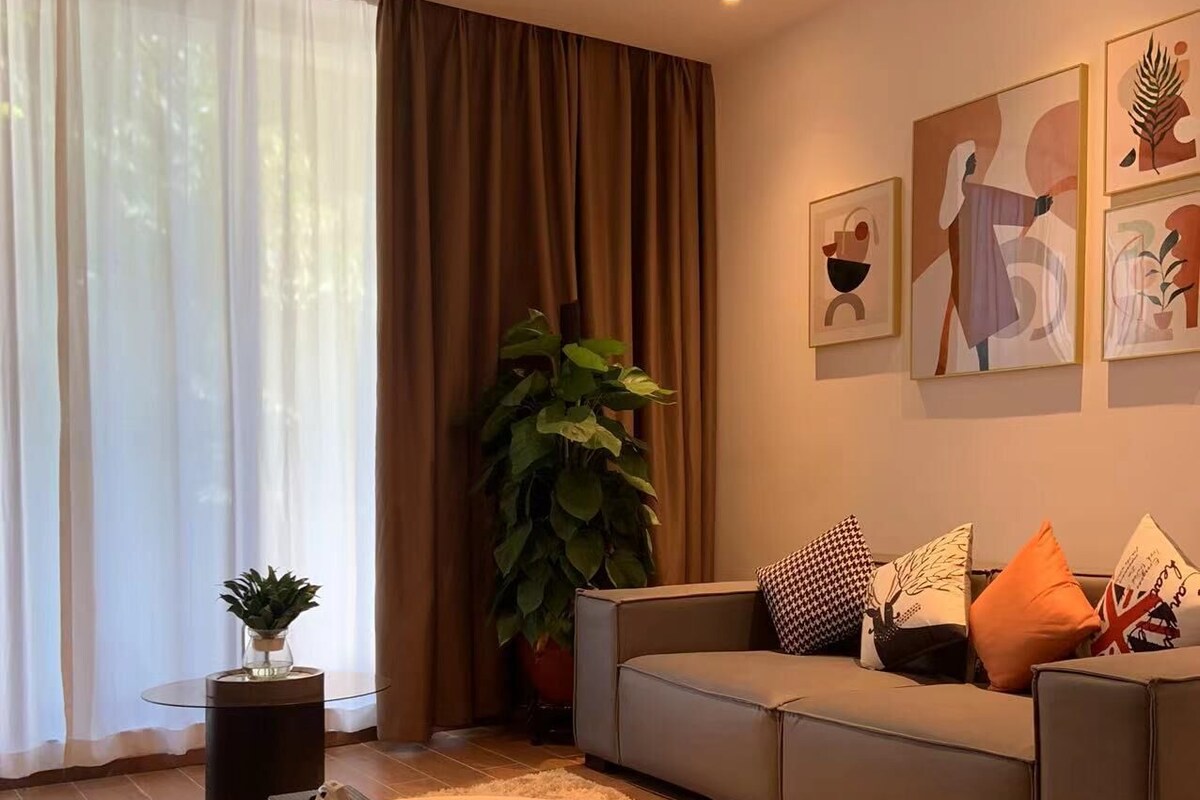 Ein modernes Wohnzimmer mit einem runden Couchtisch, einem grauen Sofa und einer großen Topfpflanze.