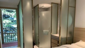 Habitación de hotel con cama, vestidor y balcón con vistas a zonas verdes.
