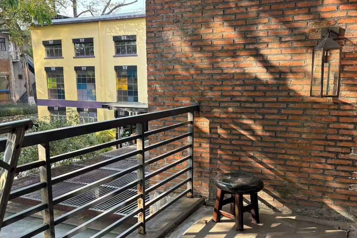 Ein Balkon mit Metallgeländer, einem kleinen Hocker und einer Ziegelwand.