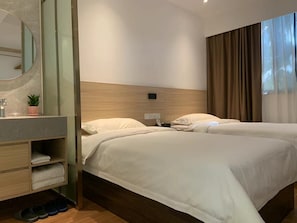 Habitación de hotel con dos camas, cabecero de madera, un espejo, un lavamanos con una planta y un zapatero.