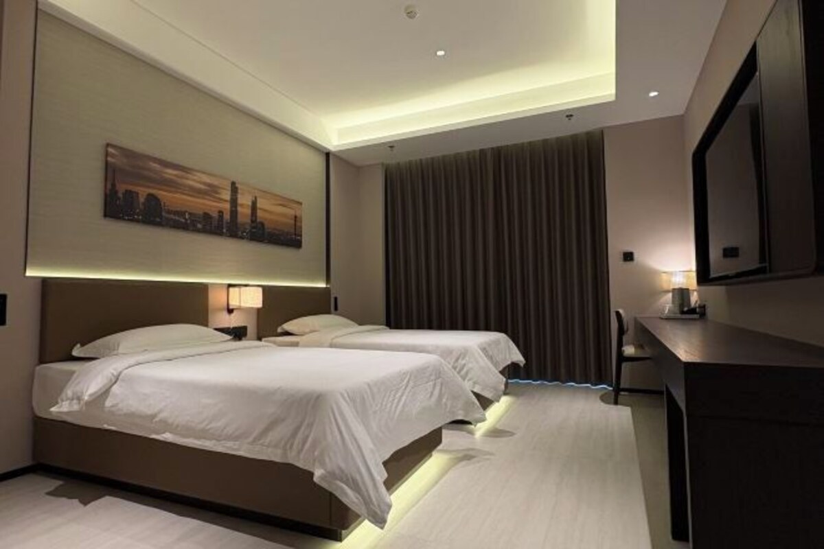 Une chambre d’hôtel avec deux lits, un bureau, une chaise, un grand miroir et un tableau au mur.