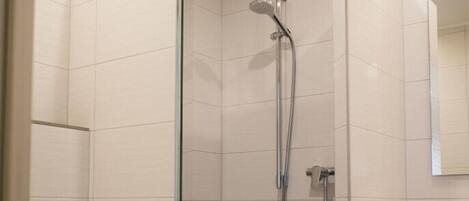 A small, modern bathroom with a glass-enclosed shower, a white toilet, and a wooden vanity with a mirror.