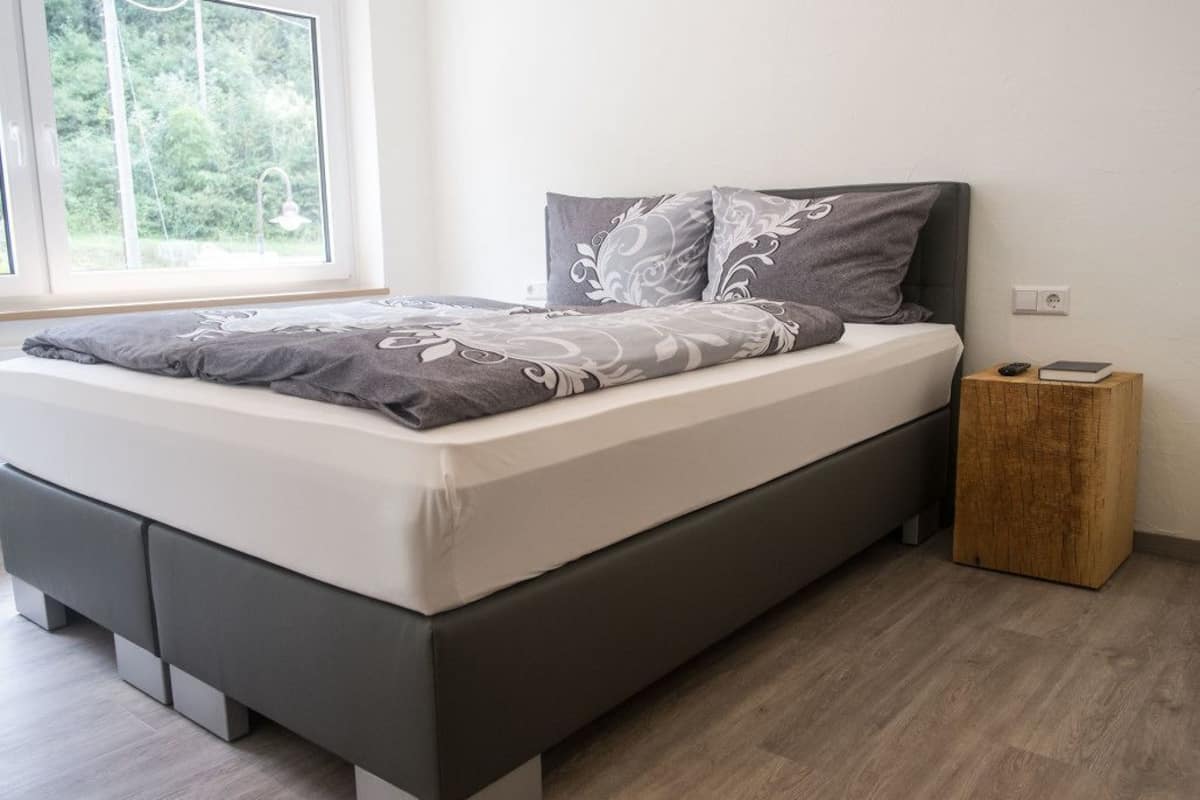 Un dormitorio moderno con cama, mesita de noche y ventana con vistas a zonas verdes.