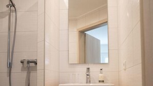 A modern bathroom with a shower, a sink with a mirror, and two towels hanging on a rack. - Hotel Haus am Berg (Pruemzurlay)