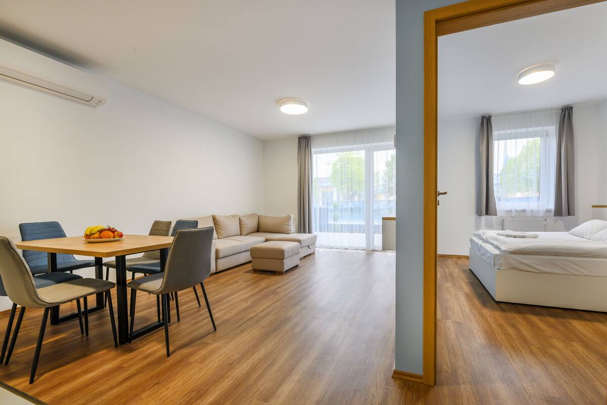 A modern hotel room with a wooden floor, a dining area with a table and chairs, a sofa, and a bed.