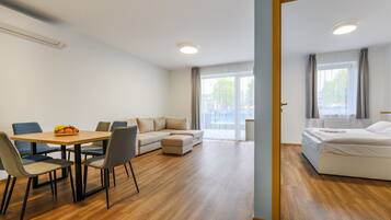 Una habitación de hotel moderna con suelo de madera, un área de comedor con mesa y sillas, un sofá y una cama.