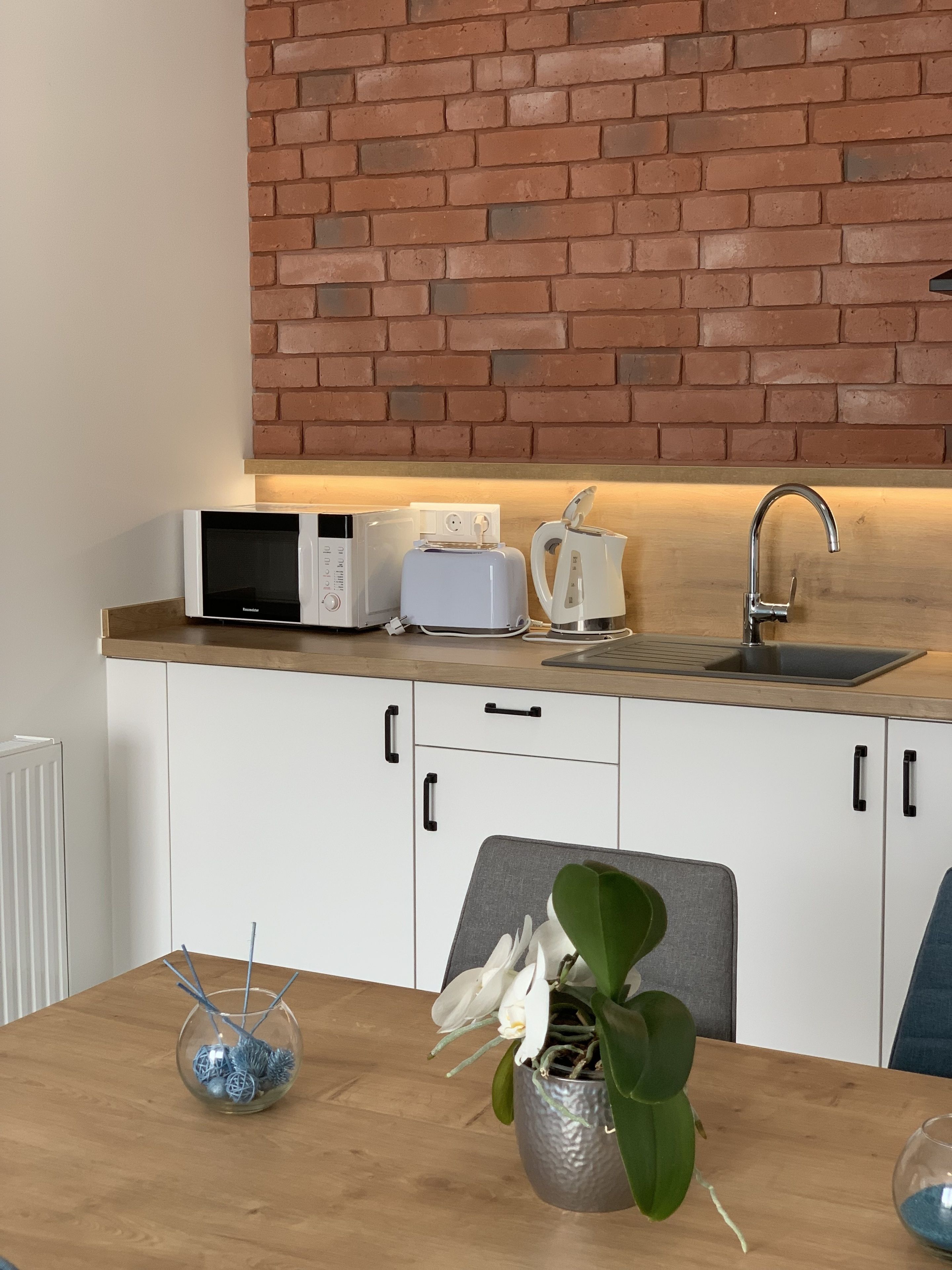 Een keuken met een bakstenen muur, witte kasten, een houten aanrecht, een magnetron, een broodrooster, een waterkoker en een spoelbak.