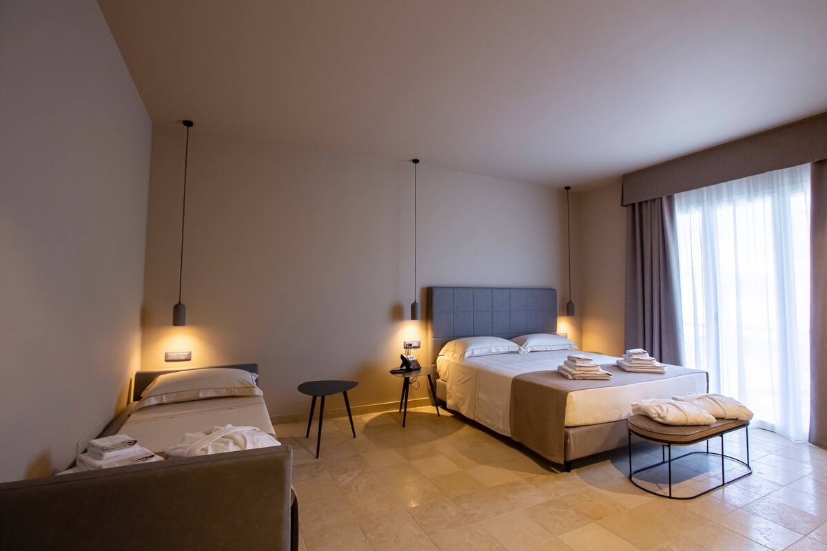 Habitación de hotel con cama, mesita de noche y una pequeña zona de estar.
