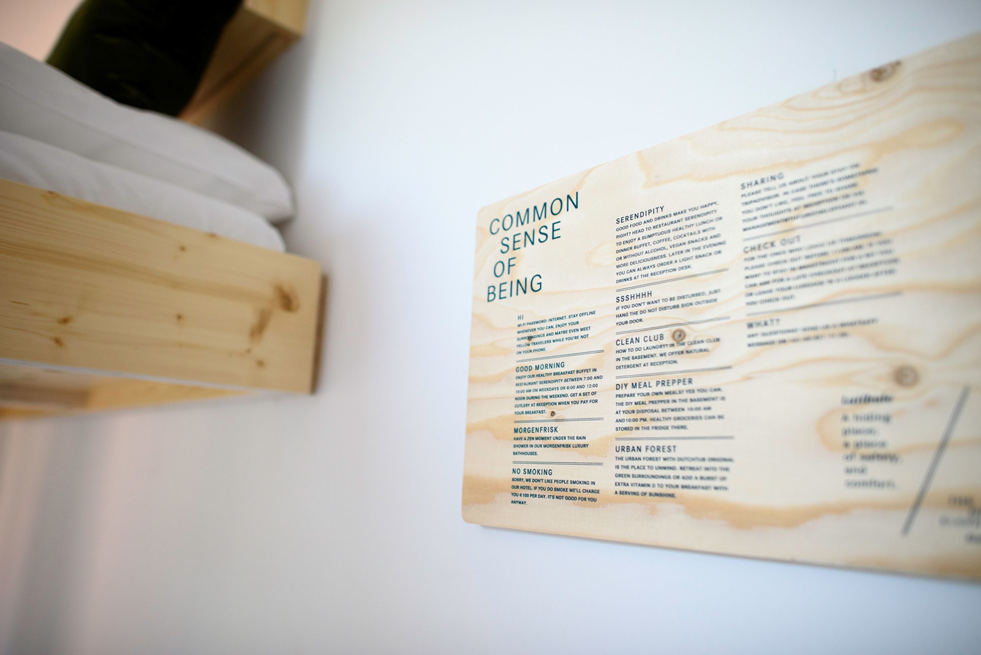 Panel de madera con texto que describe aspectos básicos de la vida, incluyendo secciones sobre casualidad, SSHHH, buenos días, morenefisk, prohibido fumar, compartir, club limpio y bosque urbano.