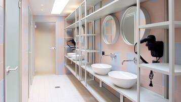 Un baño moderno con tres lavamanos, un espejo y un secador de pelo en la pared.