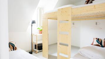 Een kamer in een studentencomplex met stapelbedden, een bureau en een plant.
