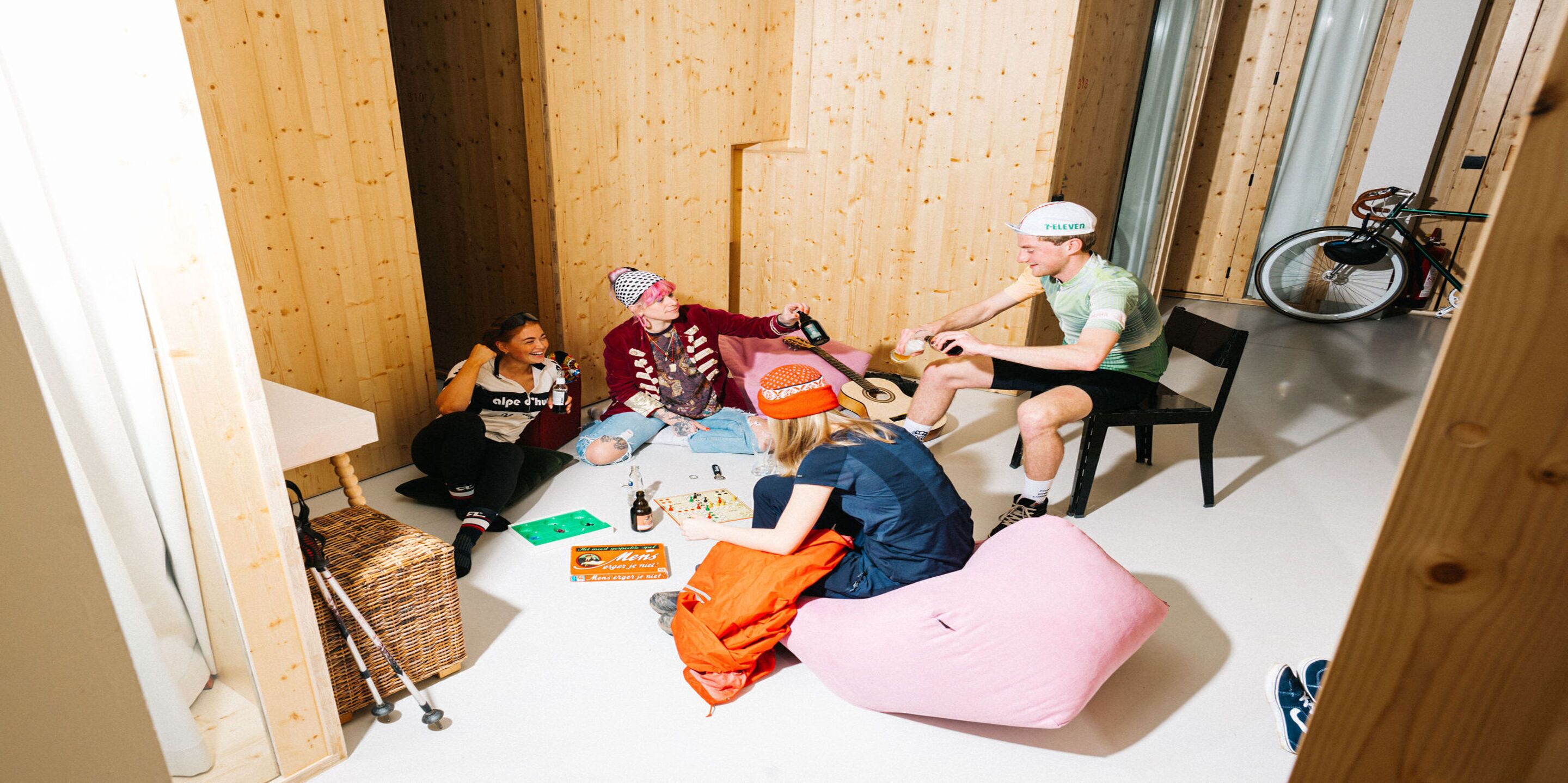 A group of people sitting on the floor in a room with wooden walls and a bicycle in the corner.