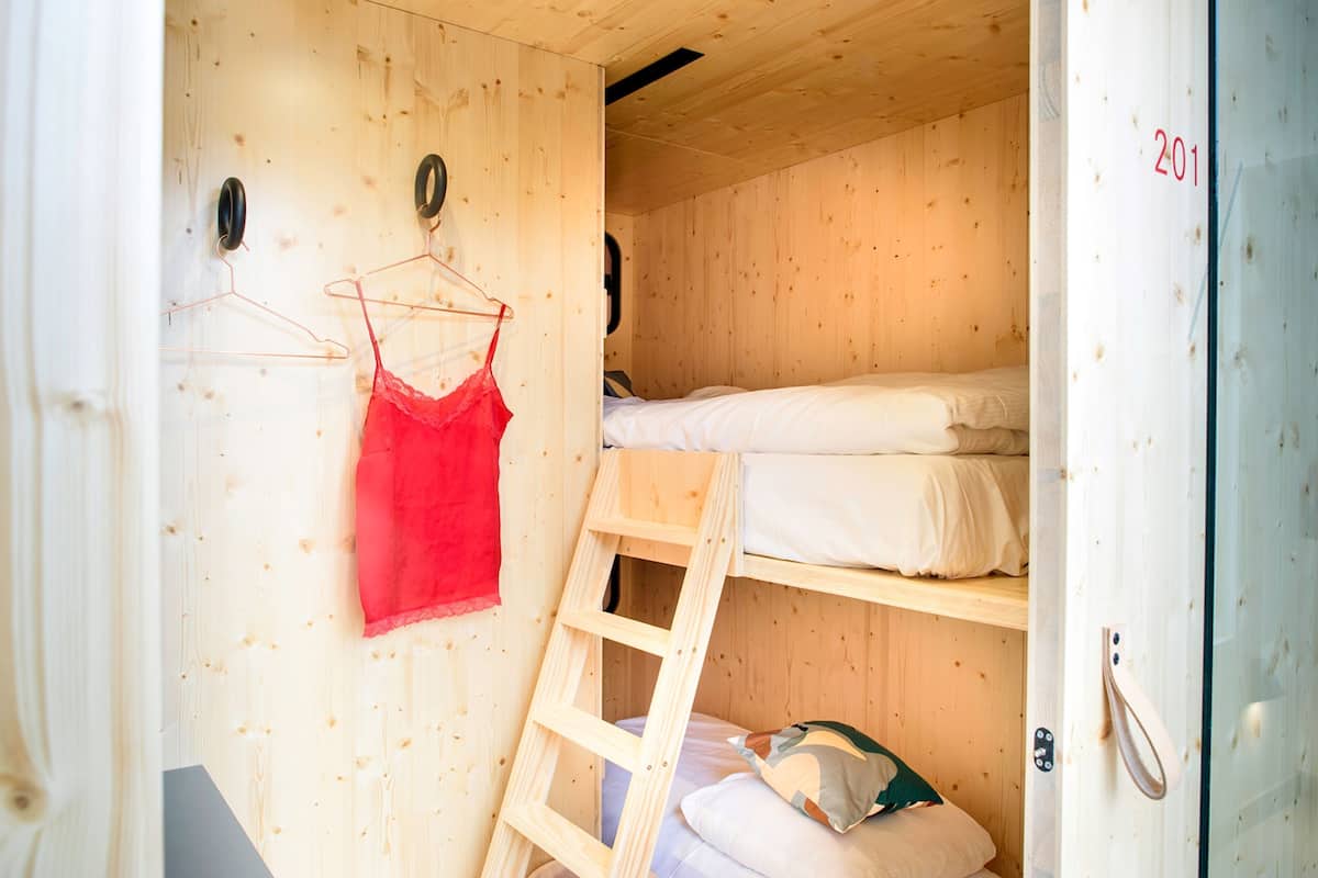 A wooden cabin room with bunk beds, a ladder, and a red garment hanging on a hanger.