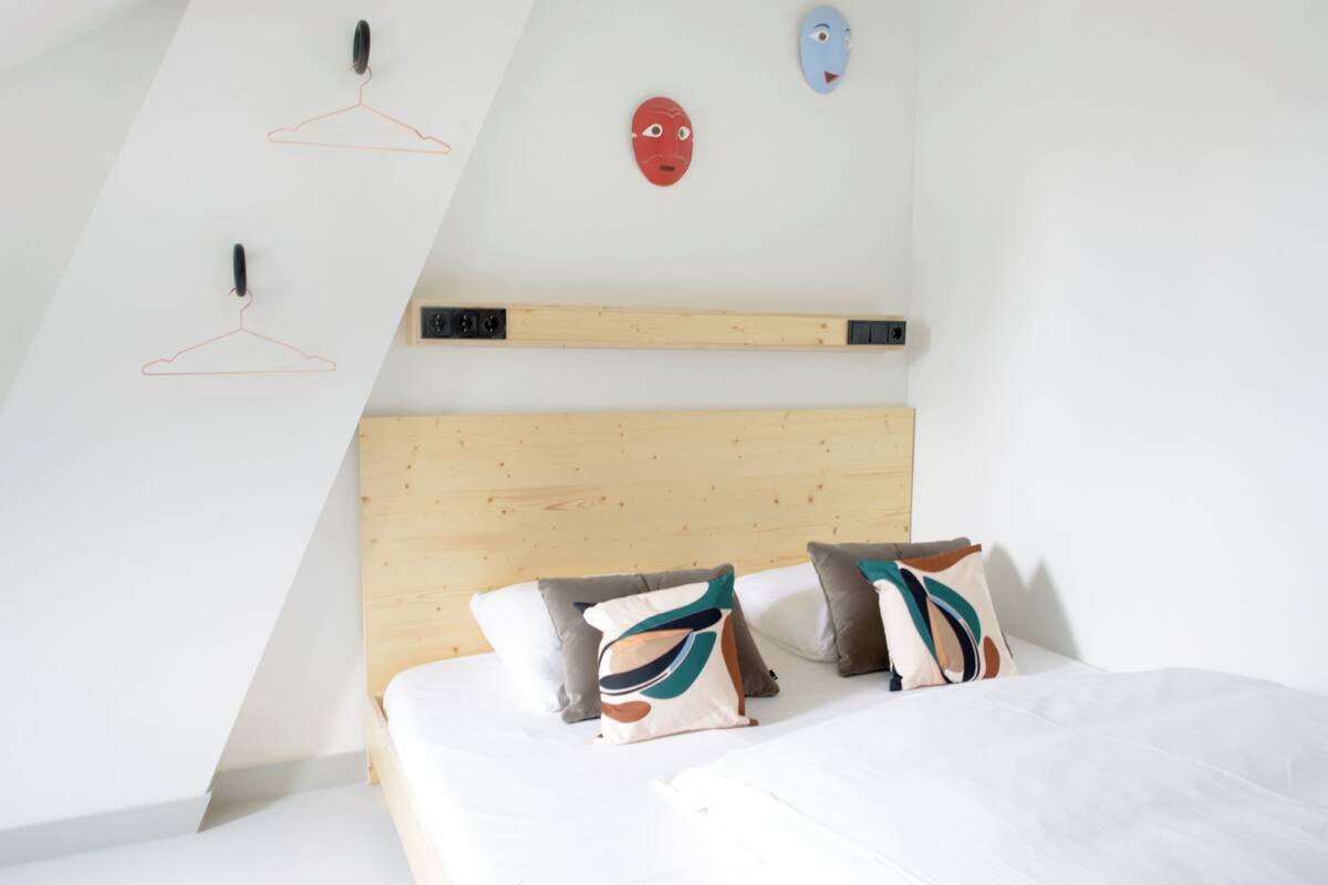 A bedroom with a wooden headboard, two pillows, and a wall-mounted shelf.