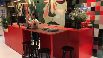 A red reception desk with black stools, a large abstract mural, and a vase with flowers.