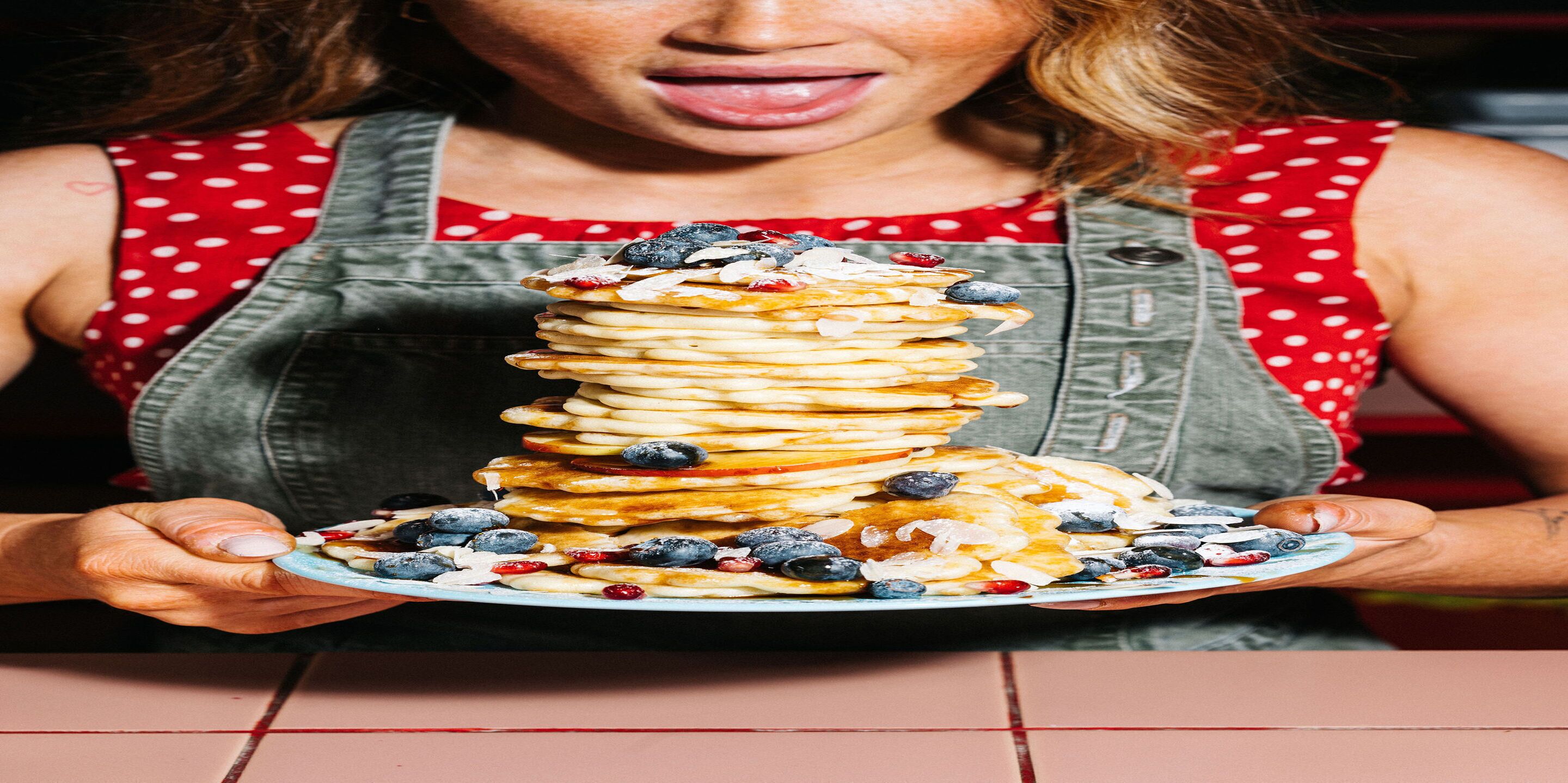 A person holding a plate of pancakes with blueberries and other toppings.