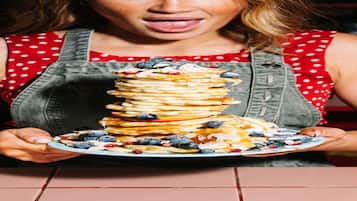 A person holding a plate of pancakes with blueberries and other toppings.