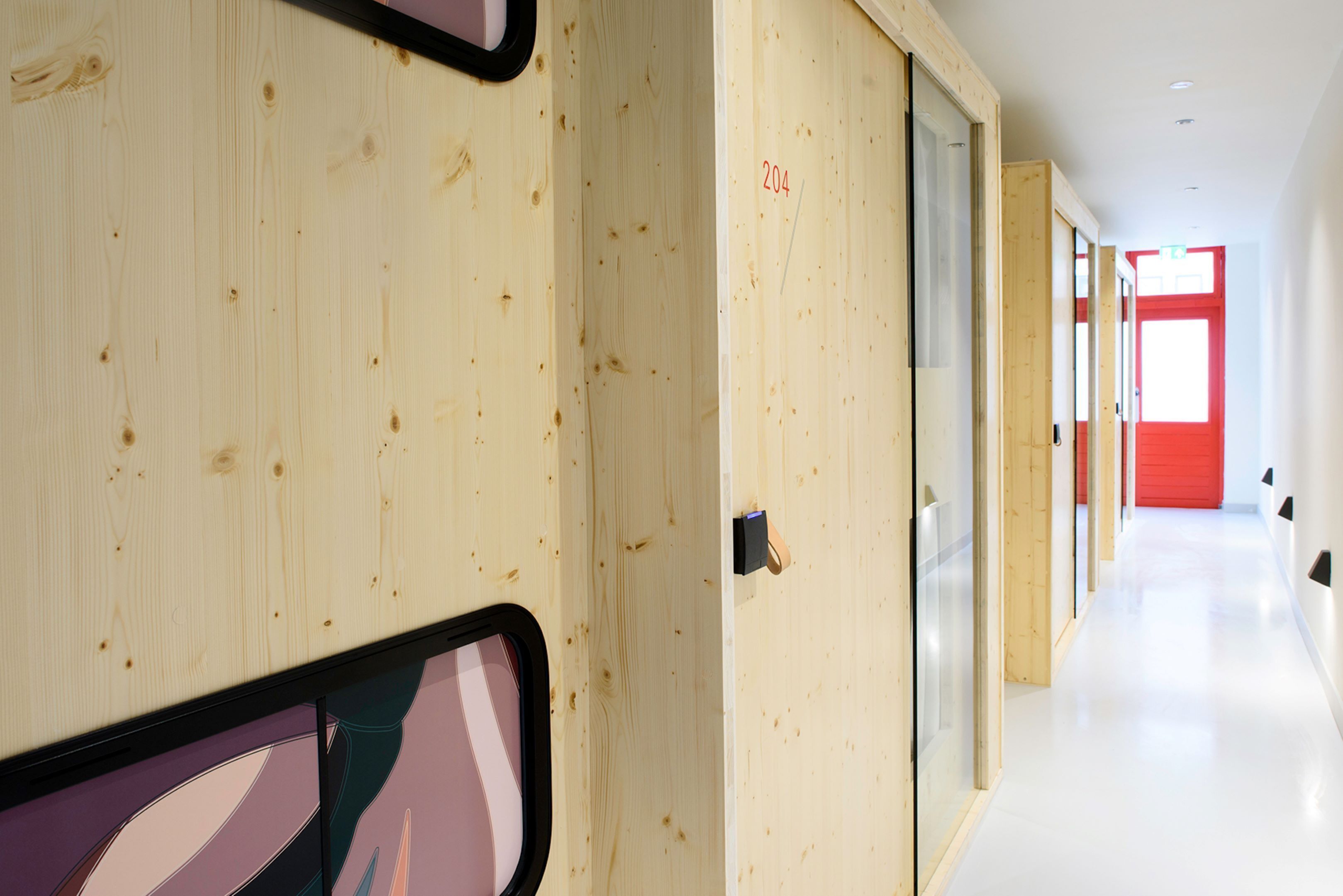 Un couloir aux murs en bois et une porte rouge au fond.