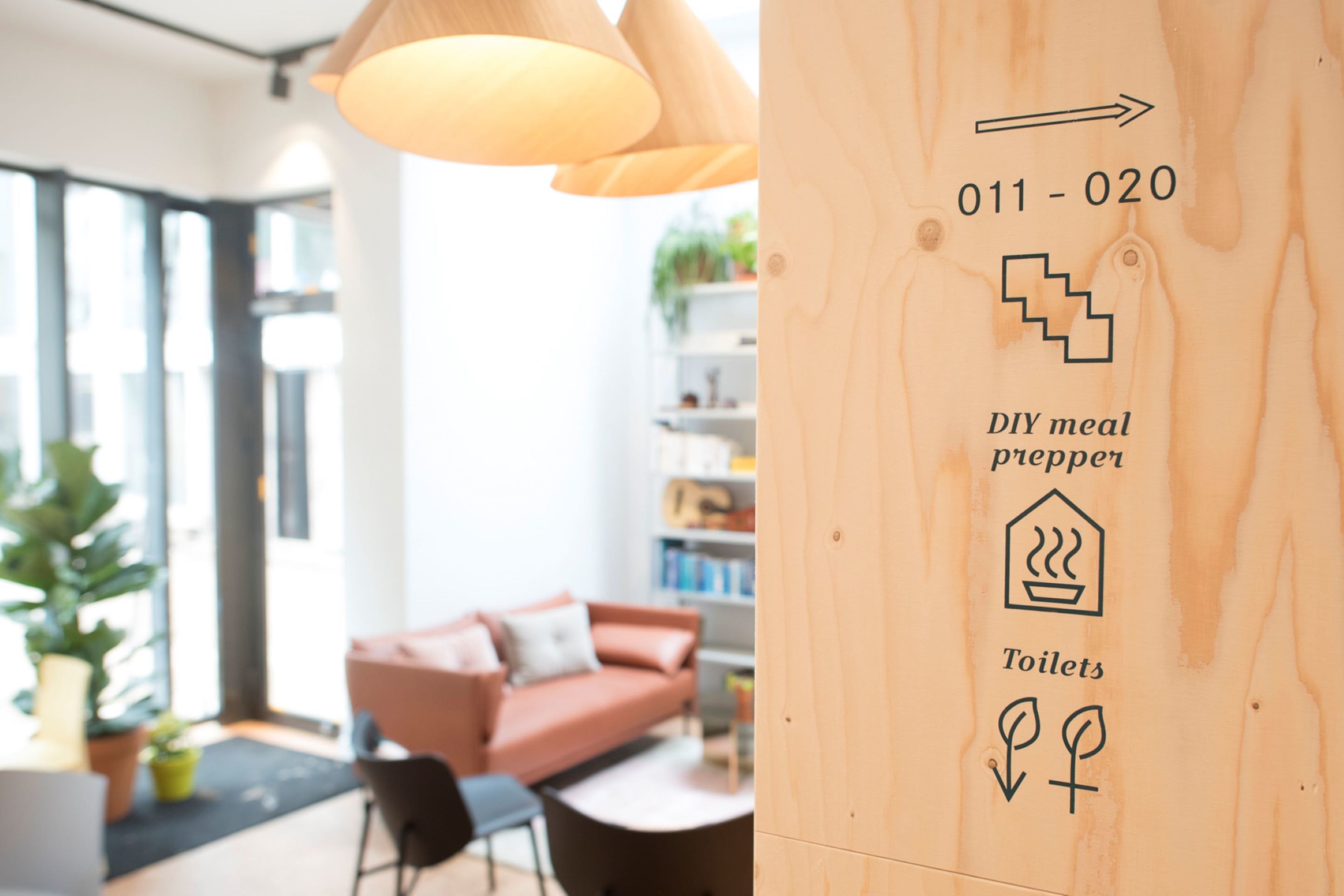A modern interior with a wooden wall displaying a DIY meal prep area, a contact number, and a symbol for toilets.