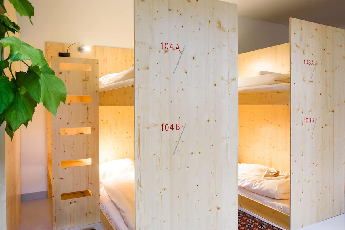 A room with bunk beds labeled 104A, 104B, 103A, and 103B, wooden walls, and a hanging plant.