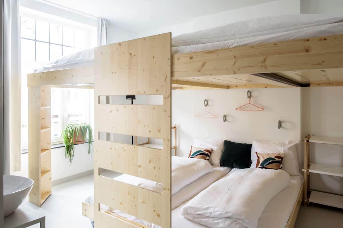 A bunk bed room with a wooden headboard, a potted plant, and a white bedspread.