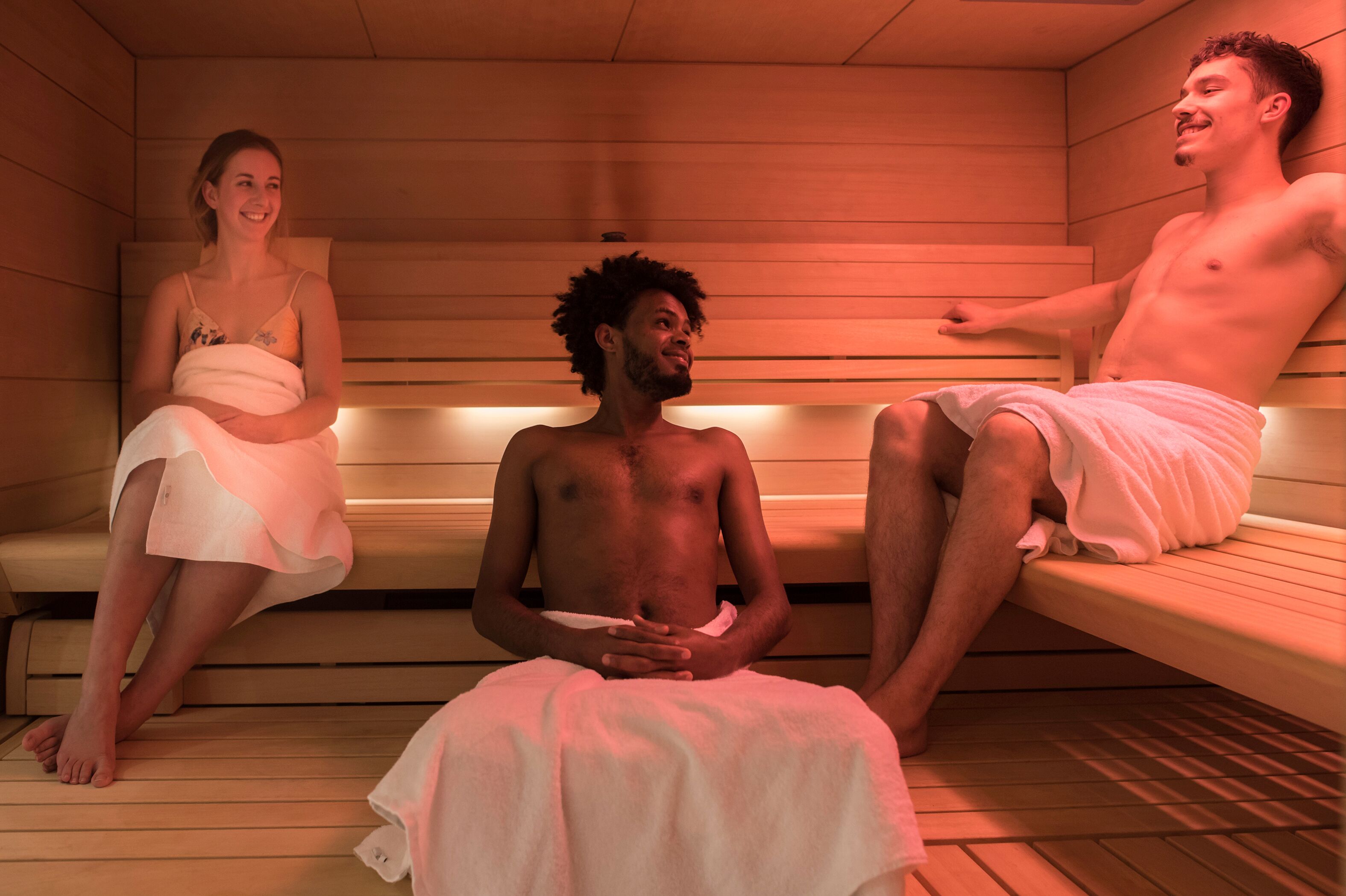 Tres persones assegudes en bancs de fusta en una sauna amb parets i bancs de fusta.
