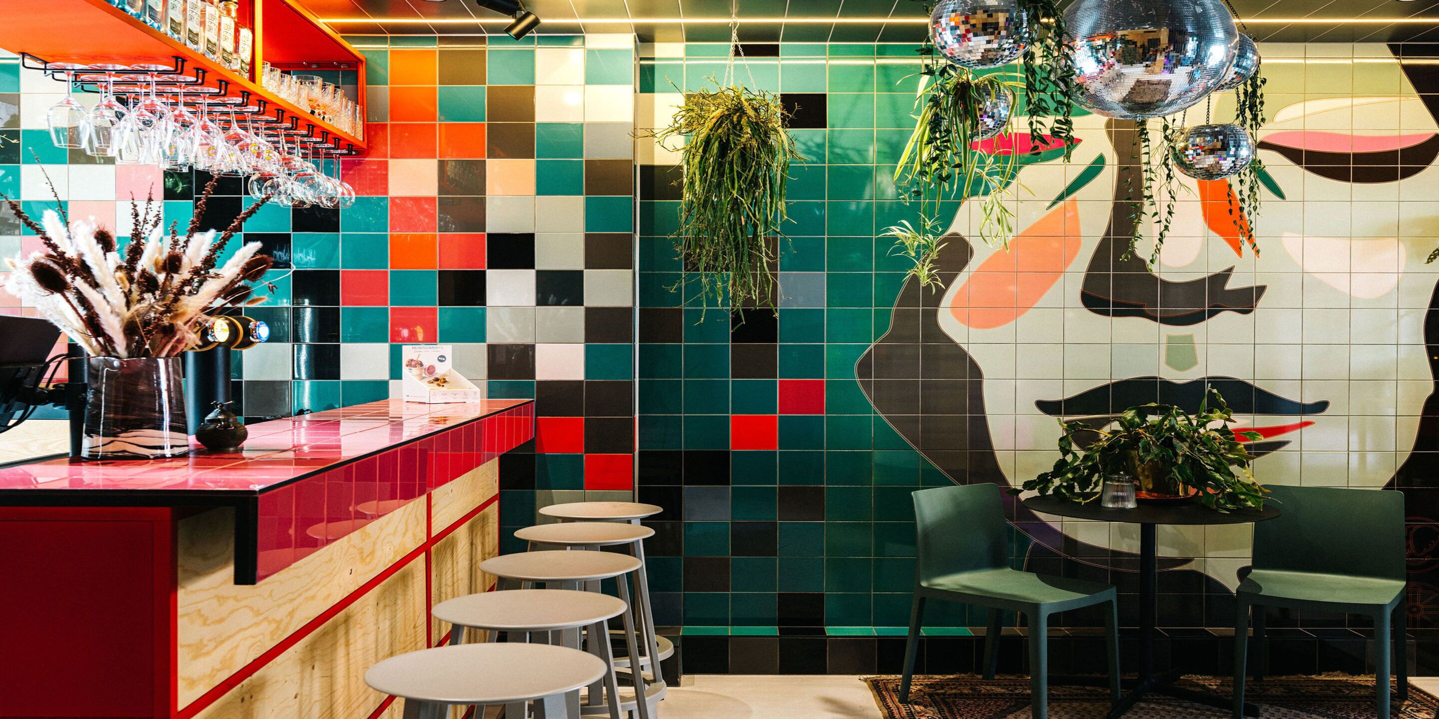 Un área de bar vibrante con baldosas de colores, una bola de discoteca y un mural de un rostro en la pared.