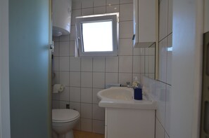 Une petite salle de bain avec des toilettes, un lavabo et une fenêtre située au-dessus du lavabo.
