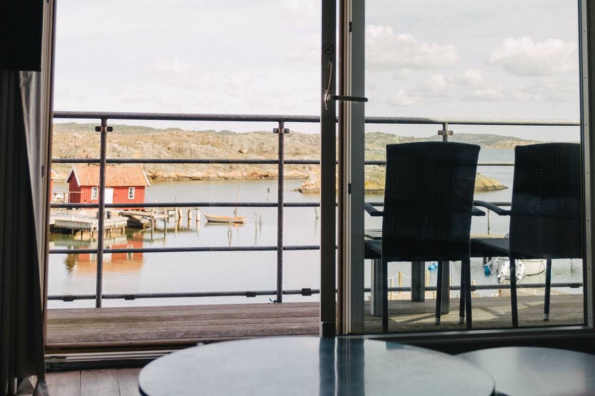 Une pièce dotée d’une grande porte-fenêtre coulissante qui donne sur un balcon offrant une vue sur une étendue d’eau et sur une côte lointaine. Il y a deux chaises sur le balcon.
