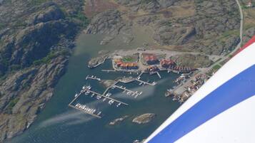 An aerial view of a coastal town with a marina, rocky terrain, and buildings with red roofs.