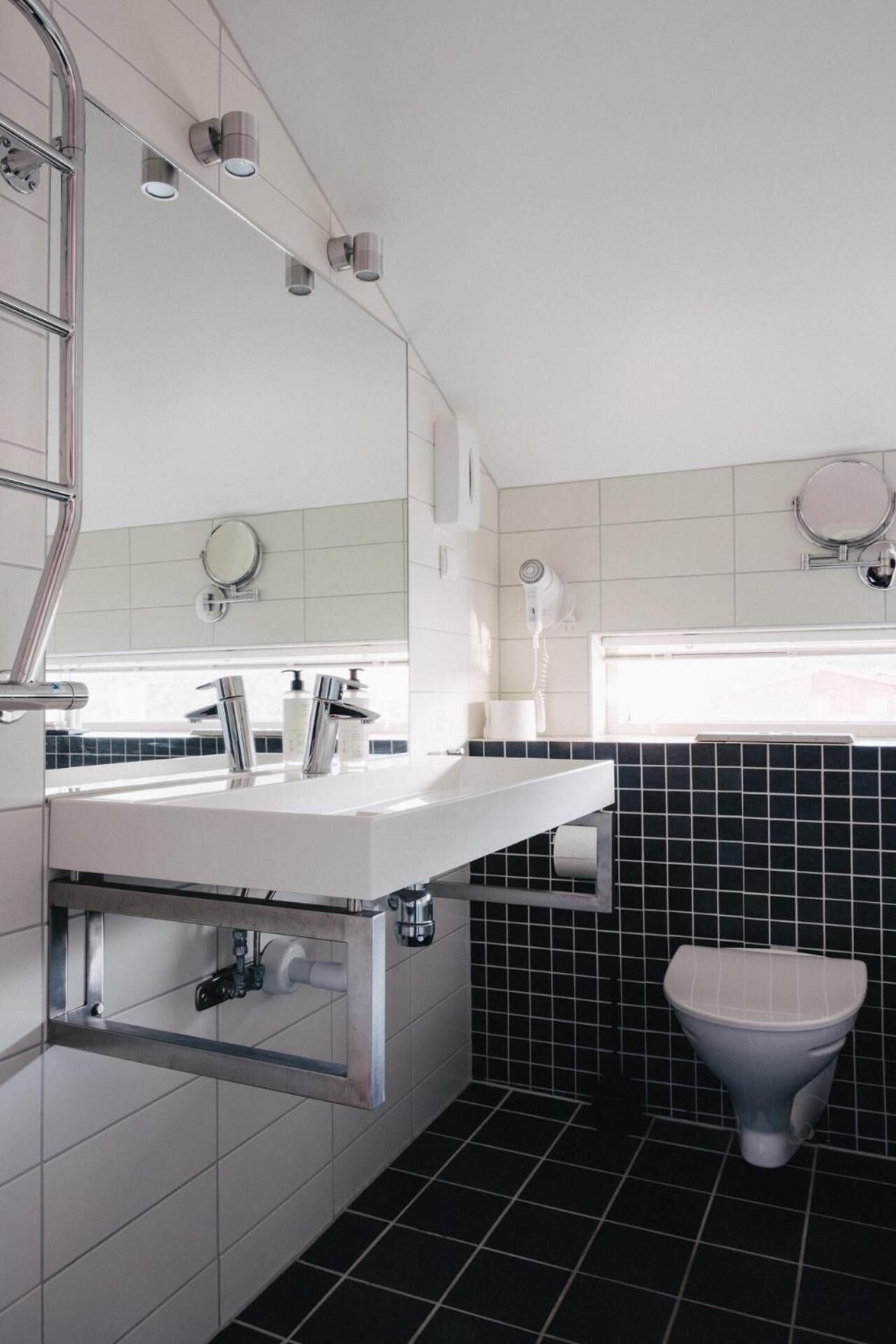 Ein modernes Badezimmer mit einem weißen Waschtisch, einer schwarzen Fliesenwand und einer weißen Toilette.