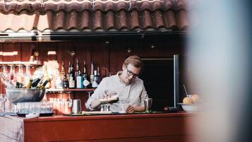 Een bar met een bartender die drankjes bereidt, diverse flessen en glazen op de planken, en een rustieke houten toonbank.