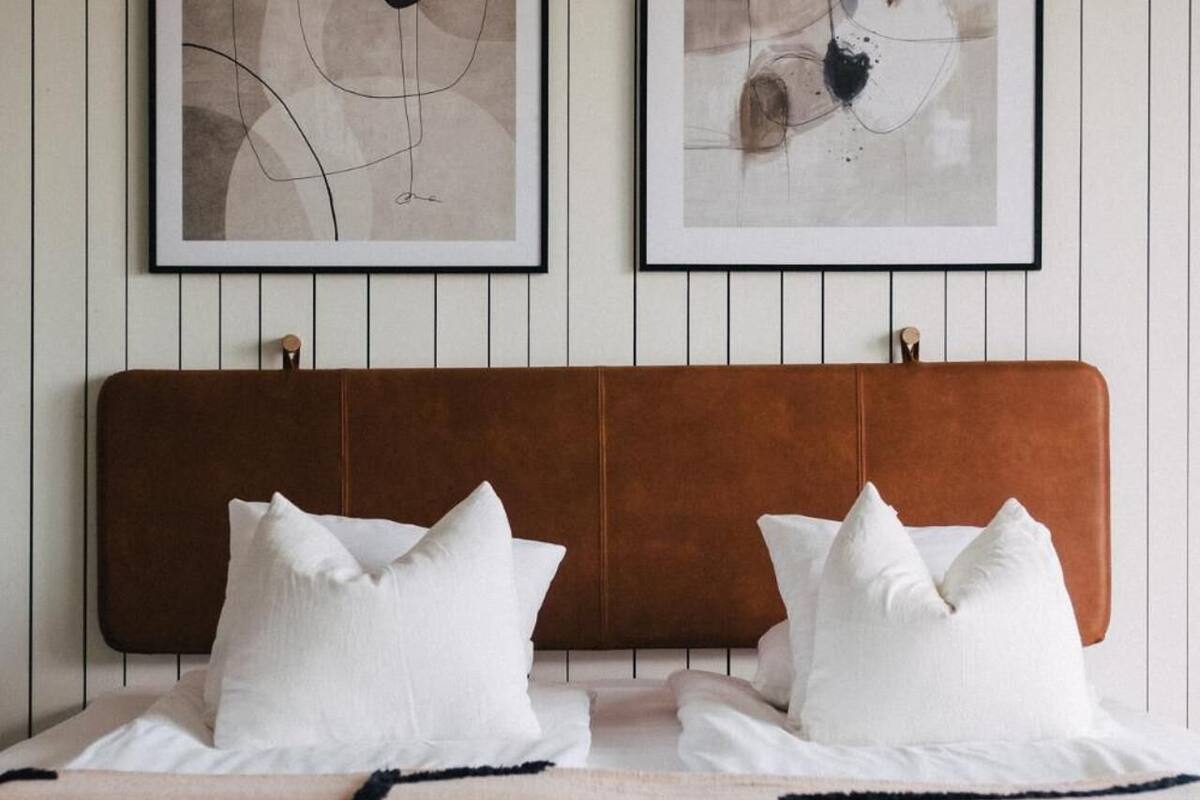 Un lit avec une tête de lit marron, deux oreillers blancs et une couverture beige.