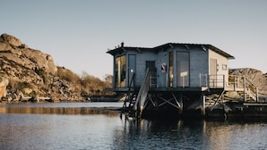 A small, elevated wooden structure with a staircase leading up to it, situated on a body of water with rocky terrain in the background. - Björholmen Hotell & Restaurang (Klovedal)