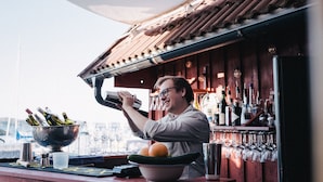 A bartender preparing drinks at a bar with a view of the city skyline. - Björholmen Hotell & Restaurang (Klovedal)