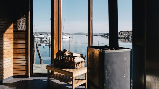 A wooden bench with a basket and a large metal container in a room with a view of a marina and boats. - Björholmen Hotell & Restaurang (Klovedal)