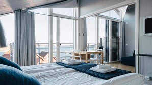 A hotel room with a large bed, a desk, and a view of the sea through large windows. - Björholmen Hotell & Restaurang (Klovedal)