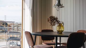 A dining area with a table and chairs, a hanging light fixture, and a view through a large window.