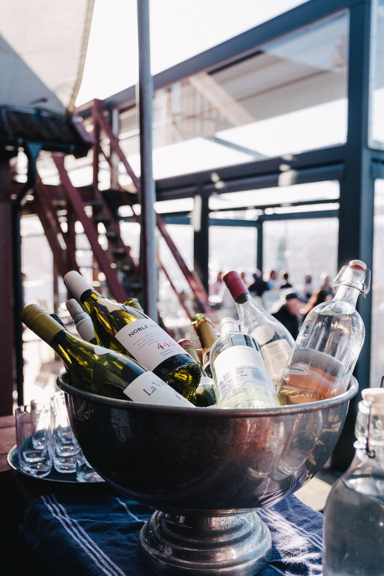 A metal bucket filled with various bottles of wine, placed on a table with a blue cloth underneath.