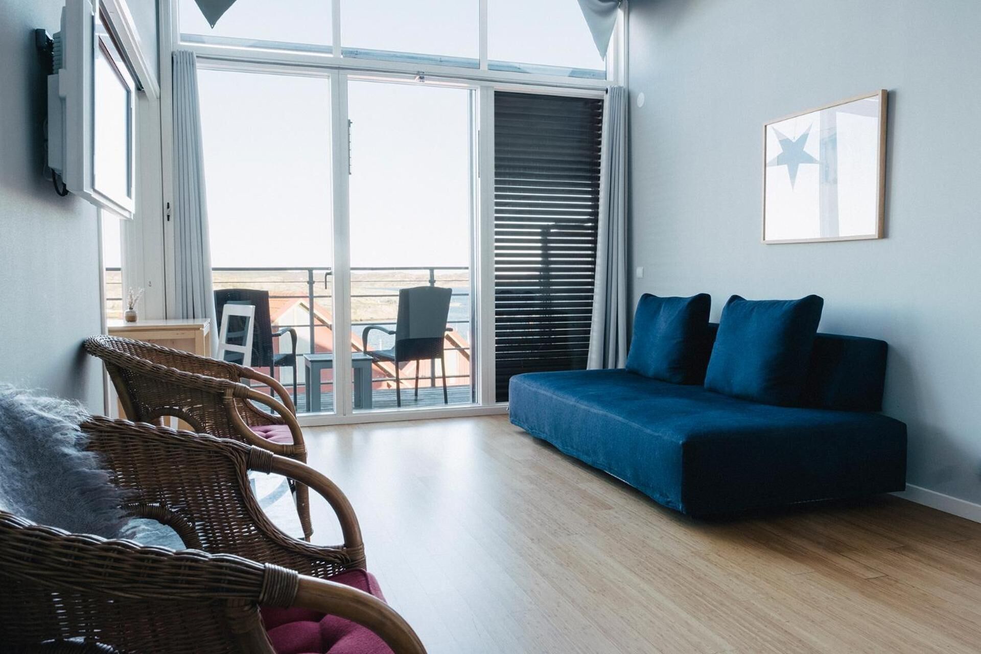 A modern living room with a blue sofa, wicker chairs, and a balcony with outdoor furniture.
